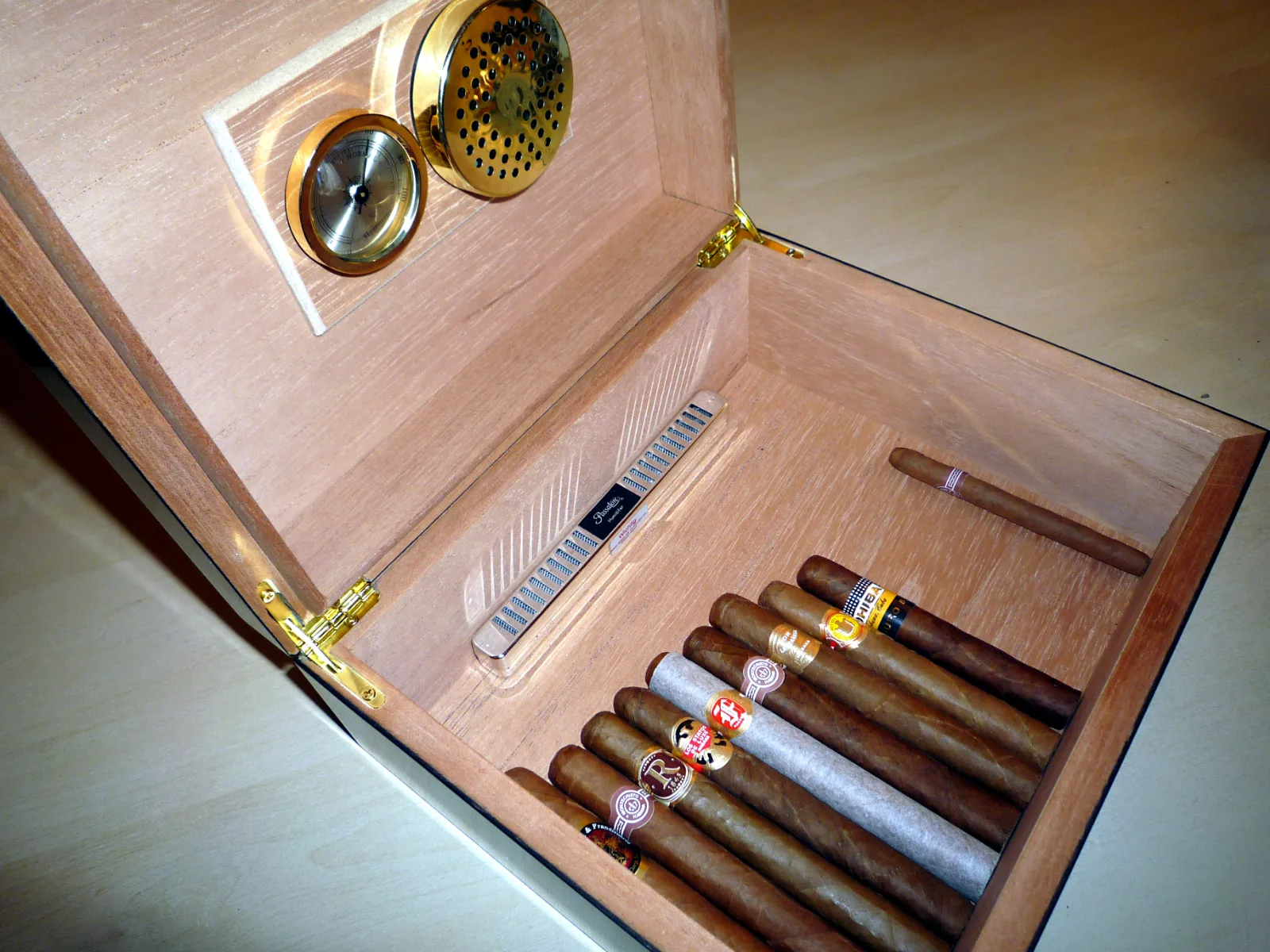 An open desktop humidor with a row of cigars inside