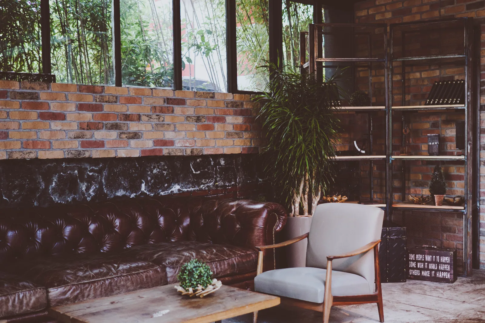 A tufted leather sofa and two armchairs against a brick wall